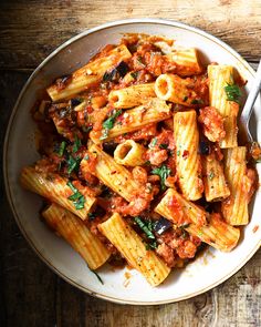 a white bowl filled with pasta and sauce on top of a wooden table next to a fork