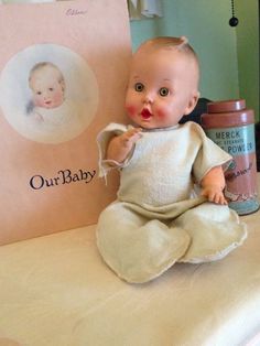 a baby doll sitting on top of a bed next to a book