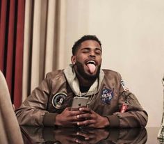 a man sitting at a table with his tongue out and holding a cell phone in front of him