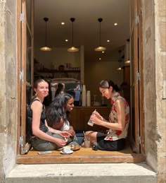 three women are sitting on the window sill and having tea in front of them