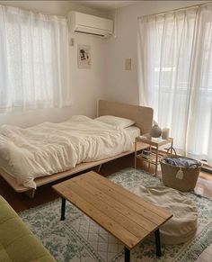 a living area with a bed, couch and coffee table in front of two windows