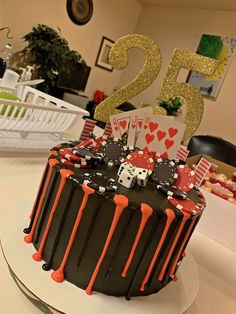 a black and red cake with orange icing on the top is decorated with playing cards