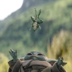 a baby yoda with two hands up in the air and another hand reaching for something