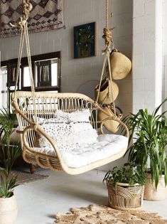 a swing chair hanging from the ceiling in a living room with potted plants and rugs on the floor