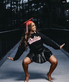 a woman in a skirt and graduation cap poses for a photo on a bridge with her arms outstretched