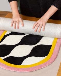 a woman rolling up a rug on top of a wooden table next to a roll of paper