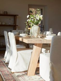 a dining room table with white chairs and flowers in vases on top of it