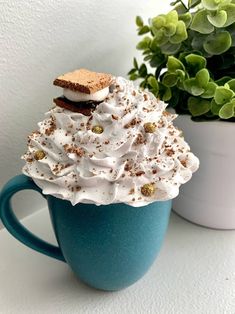 a cup filled with whipped cream next to a potted plant on top of a table