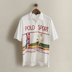 A rare item from Ralph Lauren’s athletic-themed Spring 1991 collection which featured “Polo Sport” branding prior to the official launch of Polo Sport. The colorful graphic draws inspiration from an Art Deco poster and depicts a fictitious tennis tournament held at the Ralph Lauren Tennis Club. Size medium has approximately a 30.25" back body length a 19.5" shoulder and a 46" chest. Ralph Lauren Sporty Graphic Print T-shirt, Casual Short Sleeve Polo Shirt For Tennis, White Sporty Polo Shirt With Sublimation Print, Sporty Short Sleeve Tennis Polo Shirt, Sporty Ralph Lauren Tops For Streetwear, Graphic Print Polo Shirt For Sports Events, White Graphic Print Polo Shirt For Golf, Sporty Ralph Lauren T-shirt With Graphic Print, Sporty Ralph Lauren Graphic Print Tops