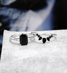 two rings with black stones on them sitting on top of a white surface, next to each other