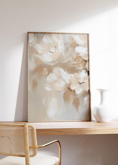 a white vase sitting on top of a wooden table next to a painting and chair