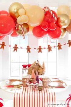 a table topped with lots of red and gold balloons next to a gingerbread house