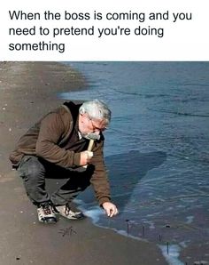 an older man kneeling down on the beach to pick up something from the water with a stick