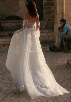 the back of a woman in a white dress walking down a cobblestone street