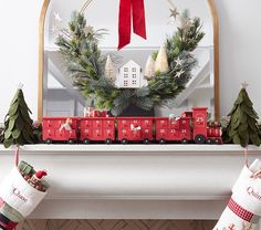 christmas stockings hanging from a mantel decorated with red train cars and evergreen wreaths