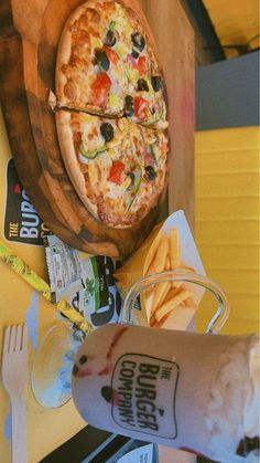 a pizza sitting on top of a wooden cutting board next to french fries and ketchup