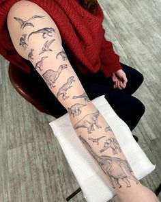 a woman sitting in a chair with a tattoo on her arm that has dinosaurs all over it