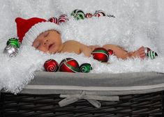 a baby is laying in a basket with christmas ornaments on it's side and wearing a santa hat