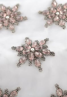 an embroidered white fabric with pink and silver flowers on the top, along with pearls