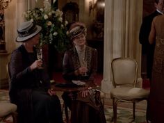 two women sitting at a table talking to each other in a room with columns and chandeliers