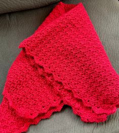 a red crocheted blanket sitting on top of a couch next to a pillow