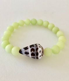 "One genuine Hawaiian cone shell stretch bracelet with 8mm quartz gemstone beads in three fun summer colors. Choose from blue lagoon, pale spring green or lavender pink. All gems are smooth dyed beads in matte colors. Hebrew cone shells are found on Hawaii's North Shore and are 3/4\" to 1\" long with characteristic brown/black square pattern on bright white. Bracelet is made to order on professional stretch elastic. When selecting size please add 3/4\" to 1\" to your actual wrist measurement for Beach Stretch Bracelet With Gemstone Beads, Beach Stretch Bracelet With Round Gemstone Beads, Natural Stones Stretch Bracelet With Round Beads For Beach, Stretch Bracelet With Gemstone Round Beads For Beach, Hebrew Cone Shell, Paris Charm Bracelet, Cone Shell, Matte Colors, Beach Bracelet