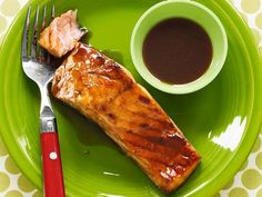 a green plate topped with meat and sauce next to a cup of coffee on top of a table