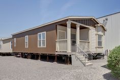 a mobile home sits in the middle of a gravel lot with stairs leading up to it