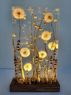 a glass vase with dandelions in it on top of a wooden base and blue background