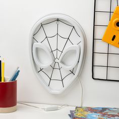 a spiderman mask mounted to the side of a wall next to a cup with pens and pencils