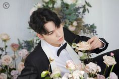 a young man in a tuxedo with flowers around his neck and hands on his lap