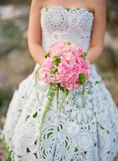 a woman in a white dress holding a bouquet of pink hydrangeas and greenery