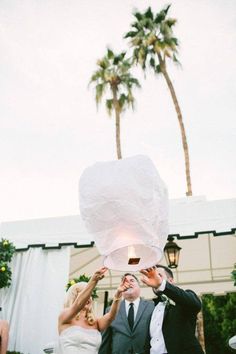 a bride and groom holding up a paper lantern