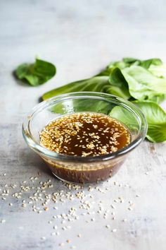 sesame seeds in a glass bowl next to lettuce leaves and seasoning on the table