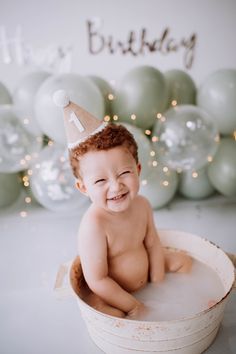 a baby sitting in a bucket with a birthday hat on