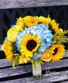 a bouquet of sunflowers and blue hydrangeas sits on a park bench