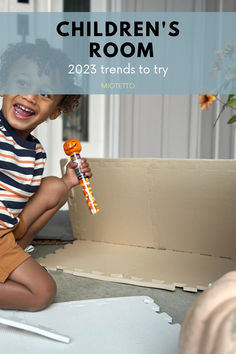 a young boy holding a candy lollipop while sitting on the floor in front of a cardboard box