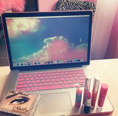 an open laptop computer sitting on top of a desk next to lipstick and makeup products