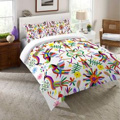 a bed with white sheets and colorful designs on the comforter, along with two nightstands