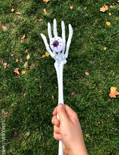 a hand holding a white plastic skeleton with an evil eye on it