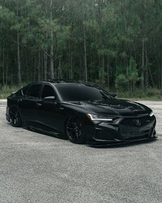 a black car is parked in the parking lot next to some tall trees and grass