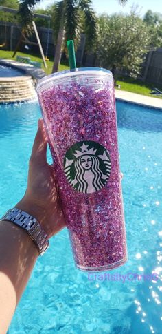 a person holding up a starbucks cup with purple sprinkles on it next to a swimming pool