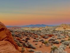 the sun is setting in the desert with rocks and plants on the ground, as seen from an overlook point