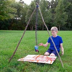 a young boy sitting on top of a grass covered field next to a painting easel