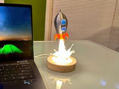 a laptop computer sitting on top of a glass table next to a rocket ship model