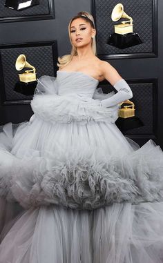 lady in grey dress standing on red carpet with awards around her neck and hands on hips