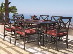 an outdoor dining table with red cushions on the patio overlooking the ocean and palm trees