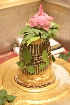 a gold vase with flowers on top of it and leaves around the base, sitting on a table