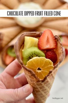 a hand holding an ice cream cone filled with sliced fruit and kiwis in it