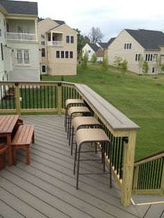 an image of a wooden deck with benches and tables on the bottom level, in front of houses